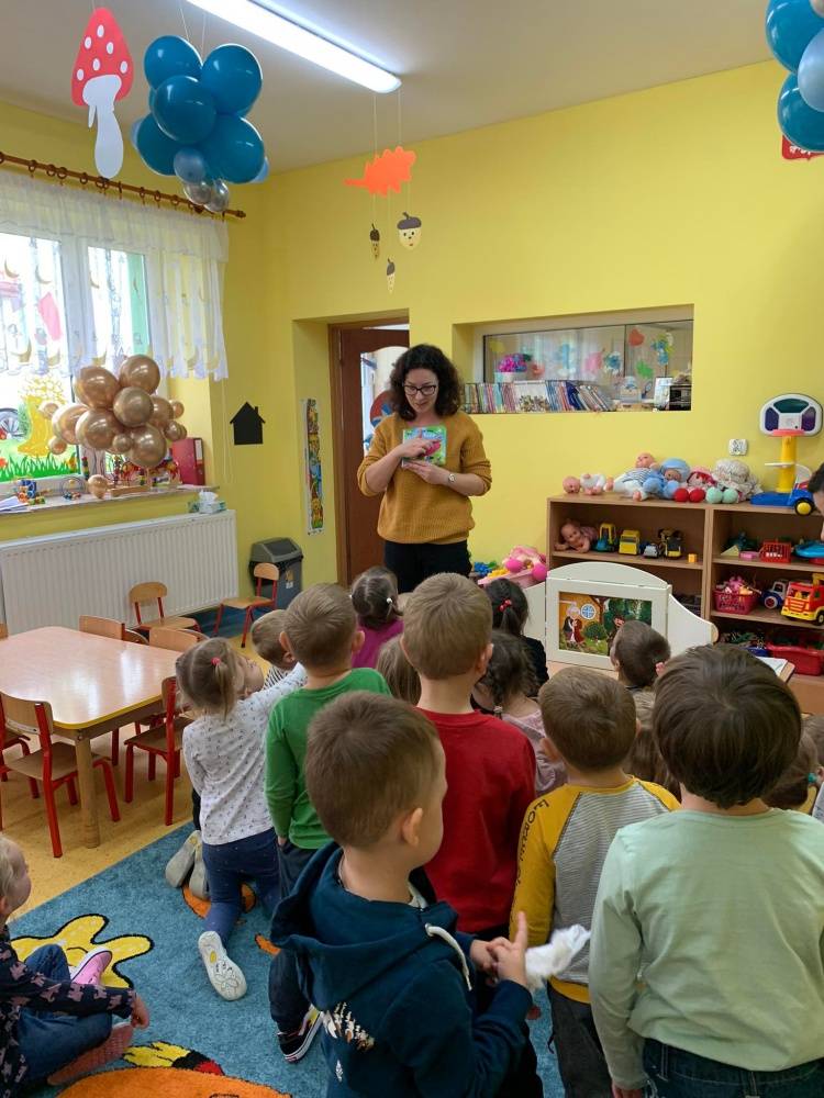 Kobieta w przedszkolu pokazuje dzieciom kolorowe książki.