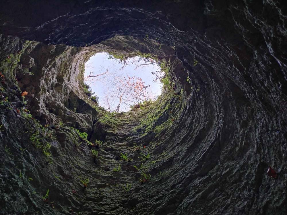 Wnętrze jaskini, w kształcie komina, z dużym otworem, w kształcie serca. Zdjęcie z dołu jaskini.
