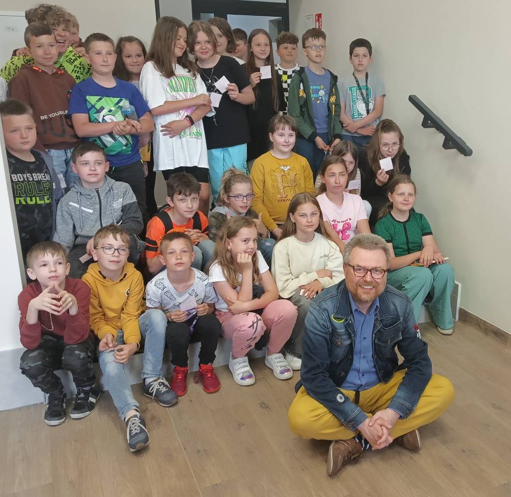 Zdjęcie grupowe uczniów klasy IV w bibliotece z zaproszonym pisarzem Marcinem Koziołem.