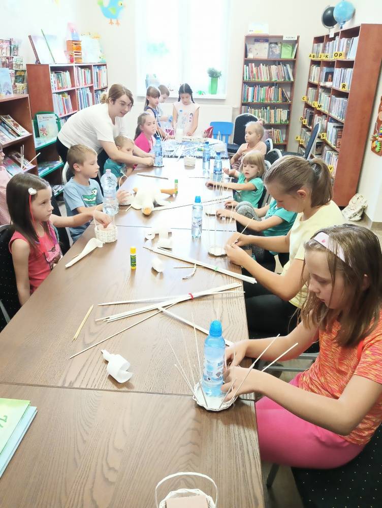 Warsztaty w bibliotece, na których dzieci wyplatają koszyczki z papierowej wikliny.