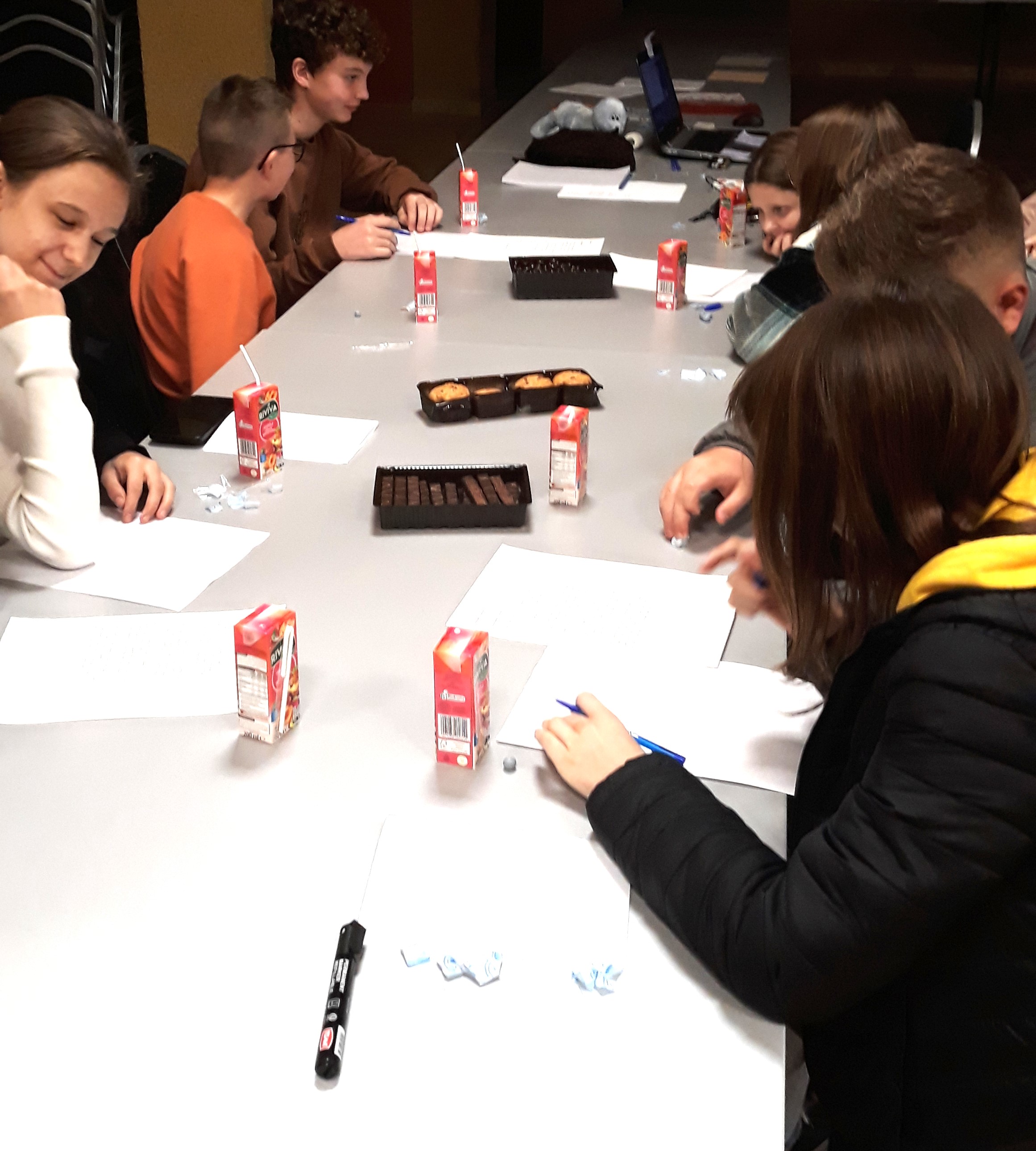 Dzieci siedzą przy stole, uczą się pisać notatki prasowe w różnych stylach.